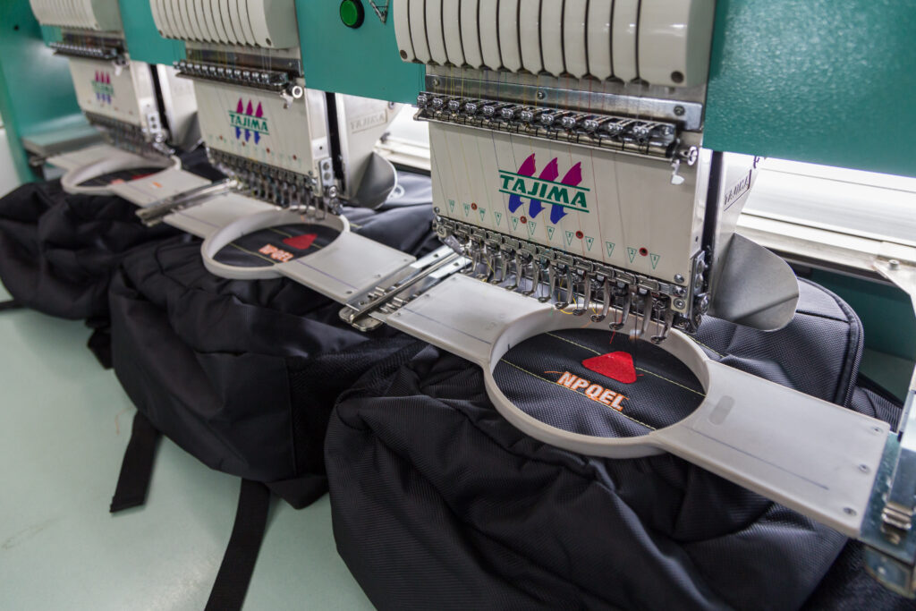 Industrial embroidery machines stitching logos on black fabric.