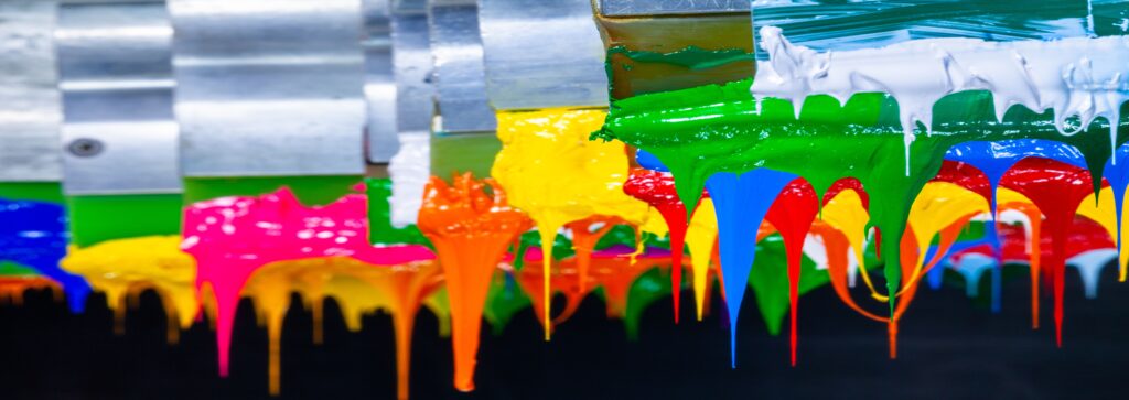 Colorful paint dripping from a metal surface in vibrant streaks.